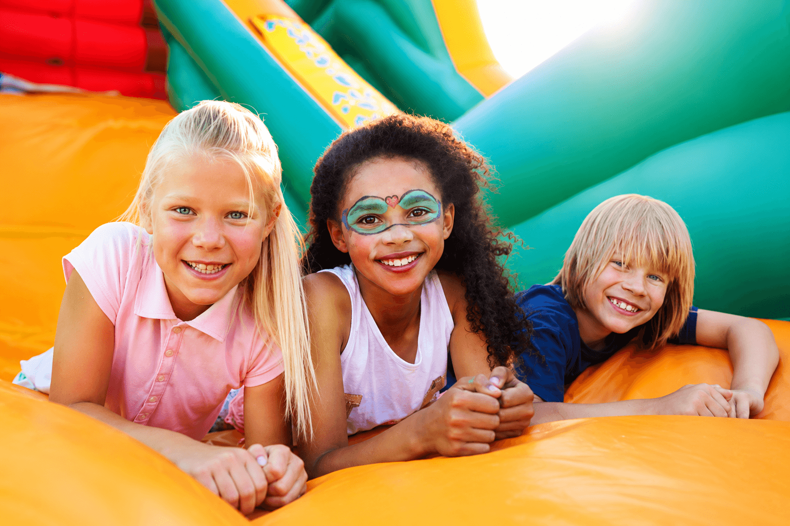 Children enjoying inflatables at a party with face paint and colorful fun